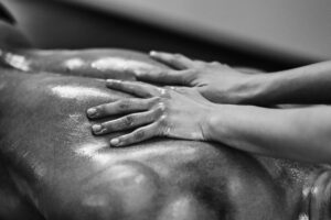 Sensual Massage NZ - Man lying down covered in oil. His back showing with a womans hands on top. Black and white image.